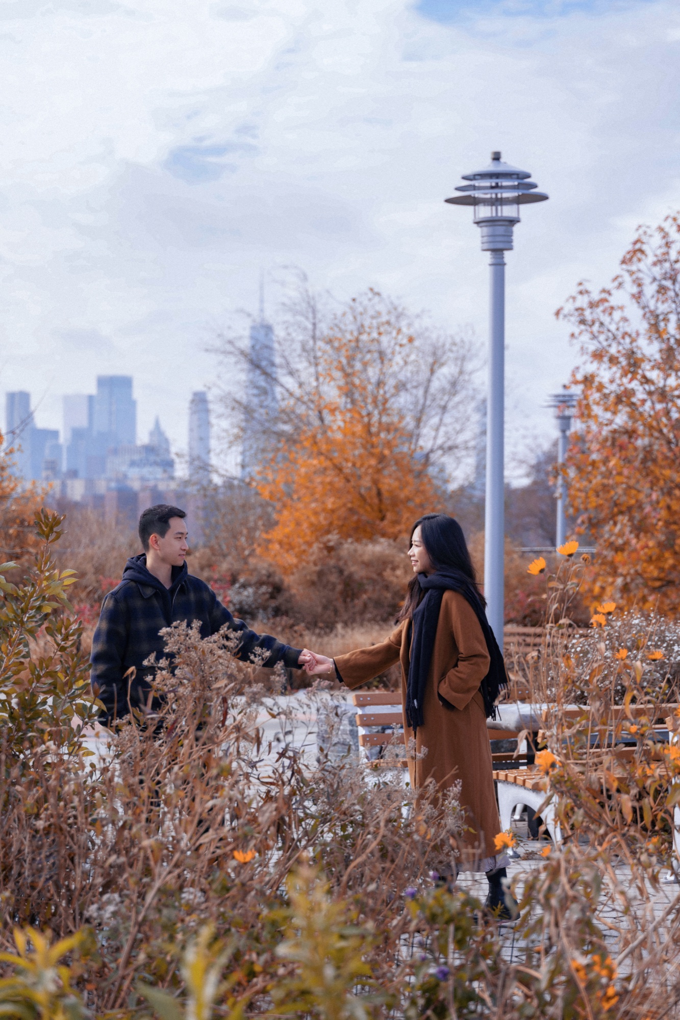 A couple holding hands among autumn plants with the city skyline behind them