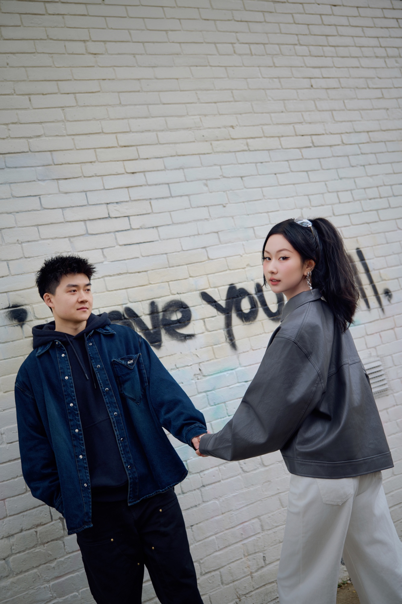 A couple holding hands beside a white brick wall