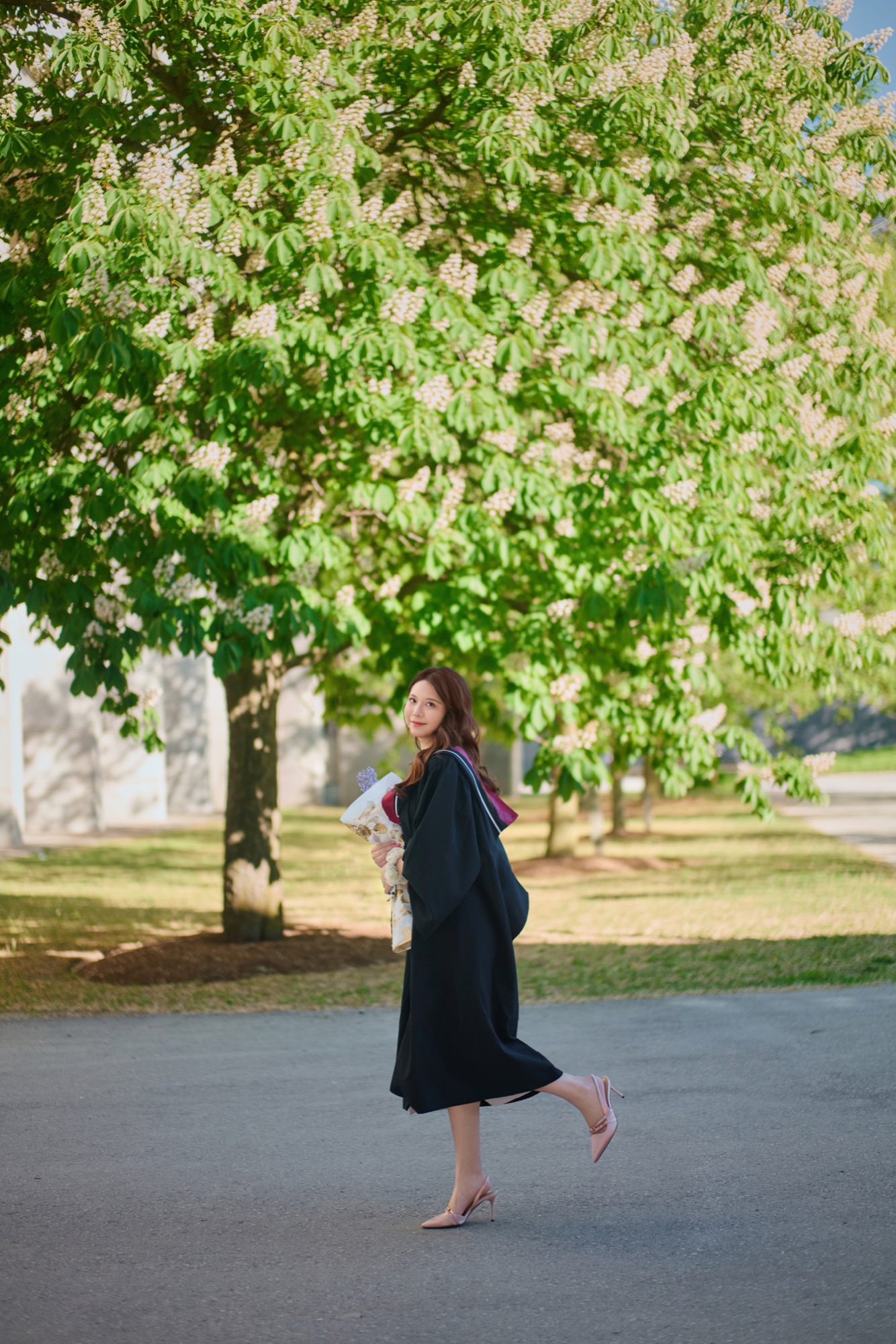 A graduate walking beneath flowering trees