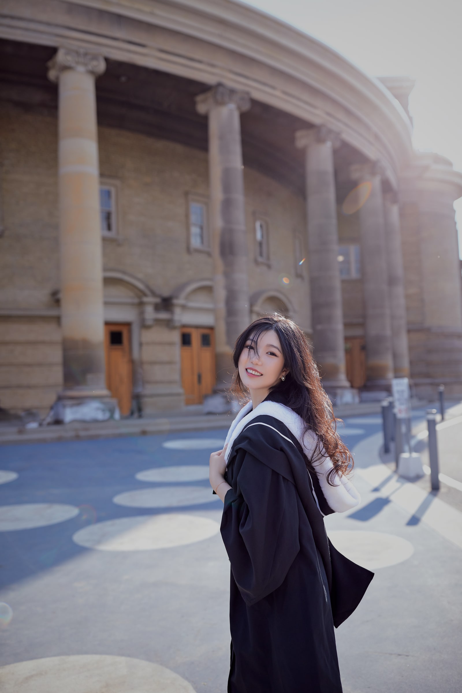 A smiling graduate looking back in sunlight before a curved row of stone columns