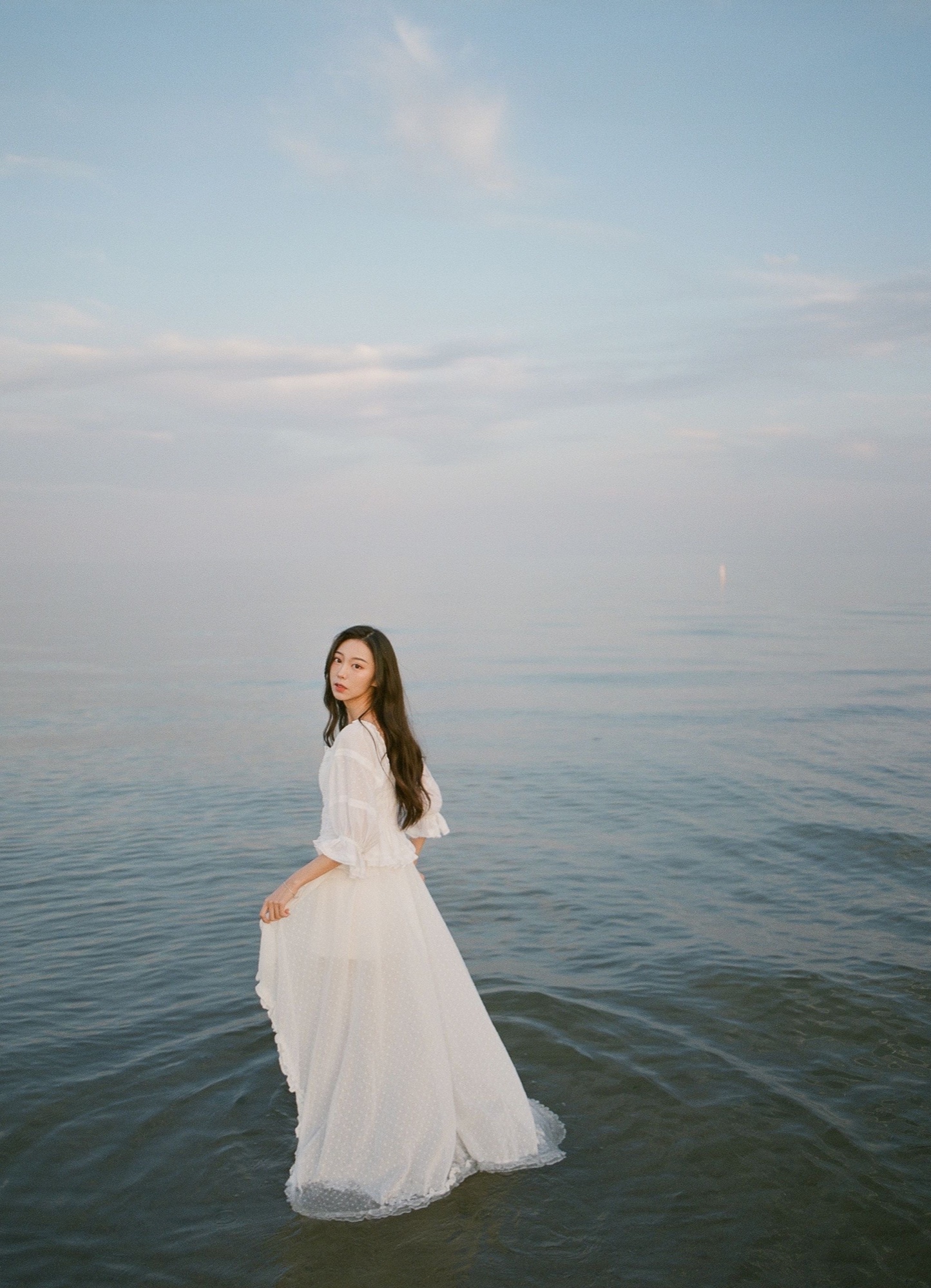A portrait in a white dress standing in still lake water