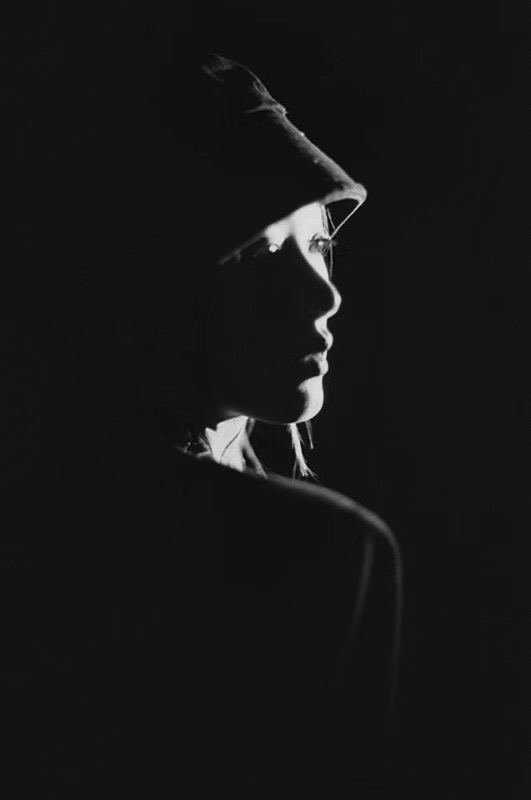 A black and white portrait in a hat, with a narrow band of light across the face