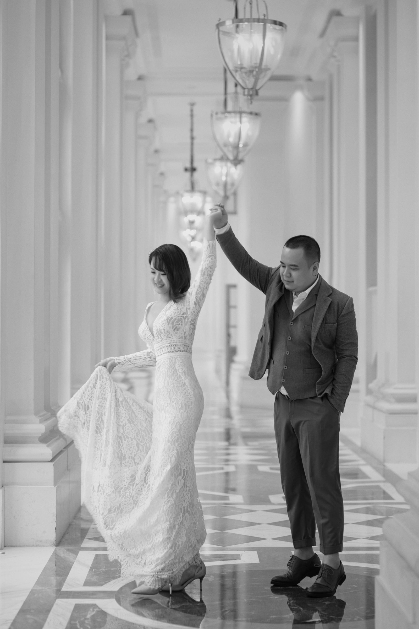 A black and white wedding photograph of a couple dancing in a columned hallway