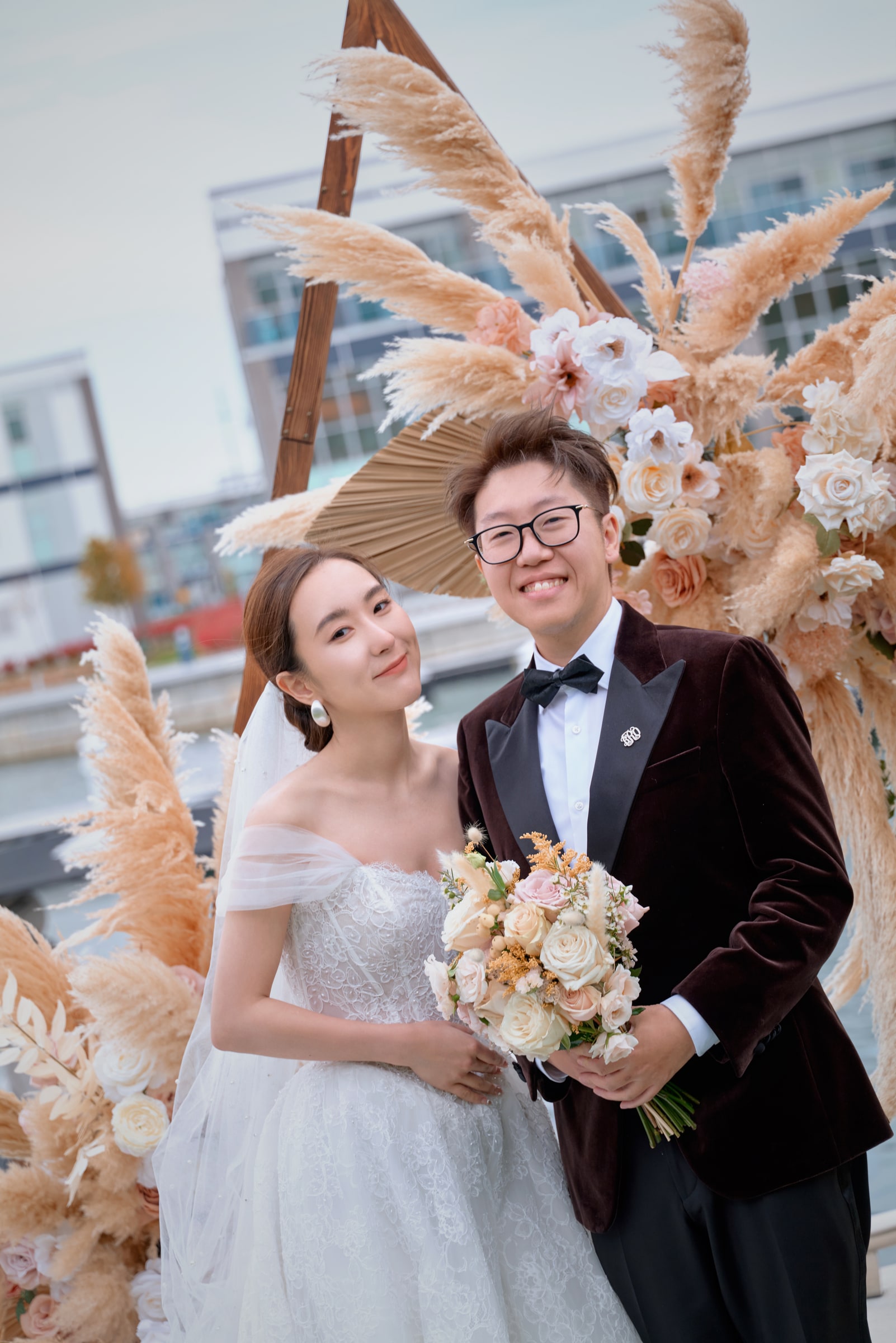 Newlyweds holding a bouquet in front of peach flowers and pampas grass
